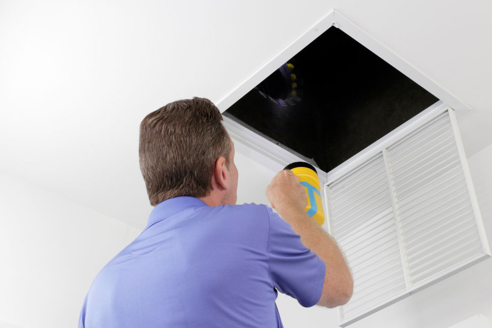 Man inspecting air duct with a flashlight